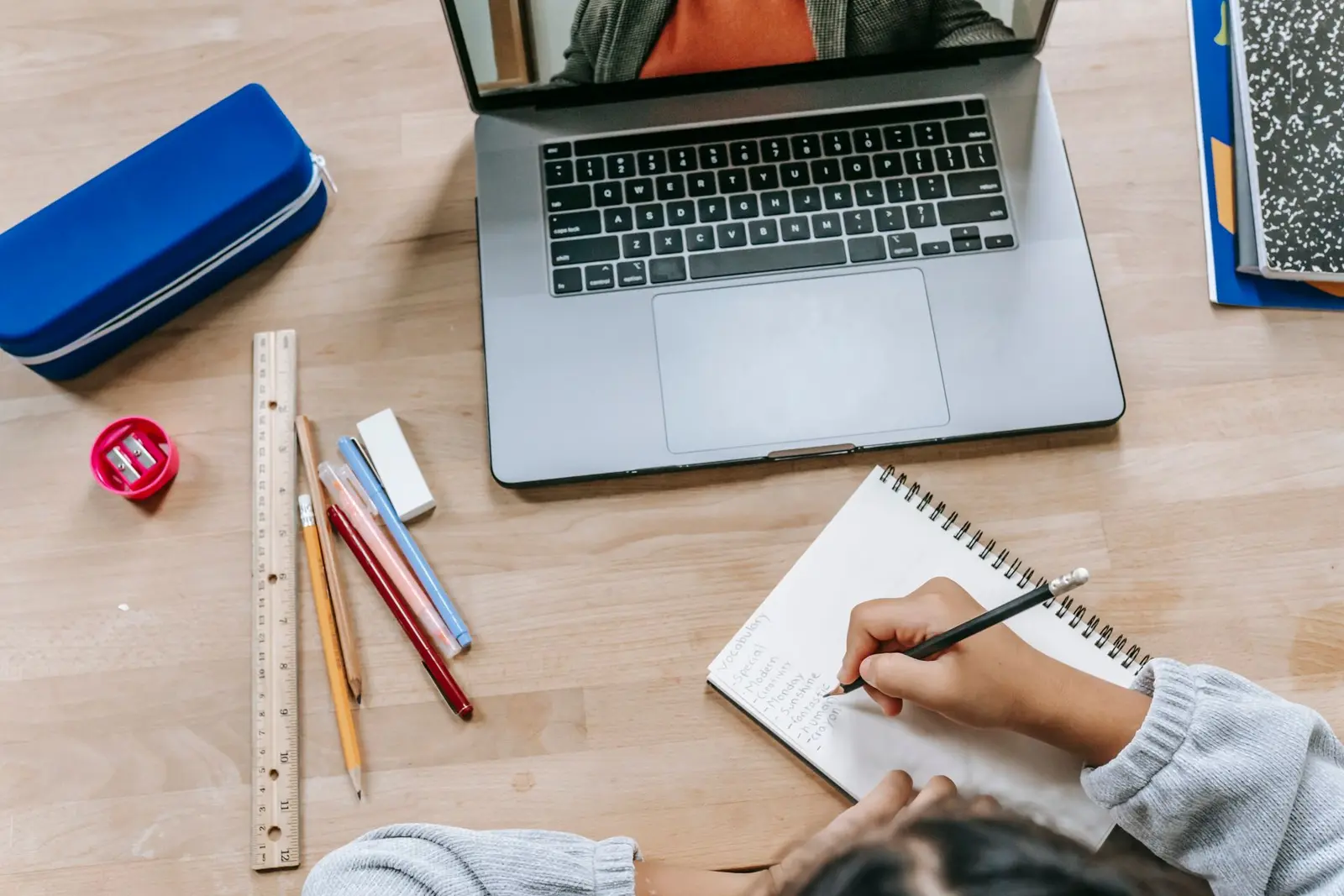 A person taking handwritten notes beside a laptop